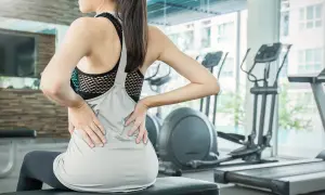 Donna in palestra con le mani sulla schiena, soffre di mal di schiena. Attenzione agli esercizi da evitare in palestra per il mal di schiena.