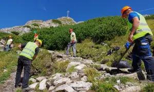 Pracownicy konserwują szlak na Giewont. Czy szlak na Giewont jest trudny? Widać krzyż na szczycie, a teren jest kamienisty.