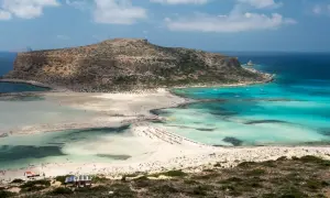 Widok na Vouisma Beach z turkusową wodą, piaszczystą plażą i skalistą górą w tle.
