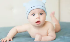 Adorable bébé garçon, prénom S, porte un bonnet bleu avec des oreilles. Il est couché sur le ventre, les yeux grands ouverts.