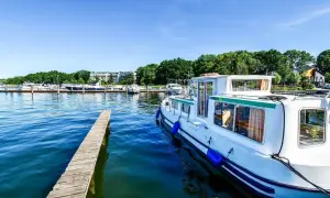 Ein Hausboot liegt im Hafen an der Mecklenburgischen Seenplatte. Ein Holzsteg führt ins klare Wasser.