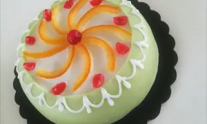 Gâteau sicilien vert pâle glacé, décoré de zestes d'orange, de fruits confits rouges et de glaçage blanc.
