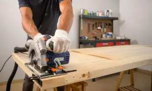 Hombre con guantes usa sierra circular para cortar una puerta de madera. Aprende como enderezar una puerta de madera con esta técnica.