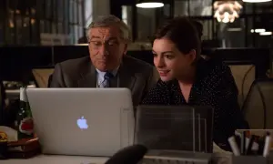 Robert De Niro i Anne Hathaway pracują przy laptopie. Młoda praktykantka z entuzjazmem analizuje dane, podczas gdy doświadczony szef czuwa nad jej pracą.