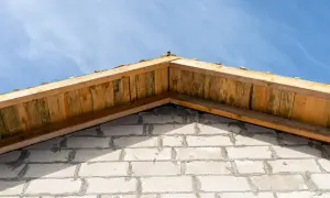 Drewniany szczyt dachu nad białą ścianą z bloczków, pod błękitnym niebem.
