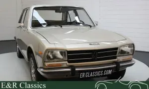 En ljusbeige Peugeot 504 står i ett garage. Bilen har en klassisk design med kromade detaljer.