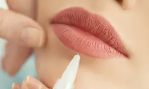 Zbliżenie na usta podczas zabiegu makijażu permanentnego. Delikatna igła zbliża się do perfekcyjnie podkreślonej linii ust.