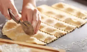 Hände schneiden mit einem Teigrädchen frische Ravioli. So einfach ist ravioli selber machen.