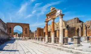 Ruines antiques de Pompéi sous un ciel bleu. Colonnes imposantes et un arc de brique invitent à visiter Pompéi et à imaginer la vie d'autrefois.