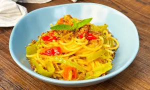 Spaghetti con friggitelli, pomodorini e mollica tostata, guarniti con basilico fresco. Un piatto semplice e gustoso.