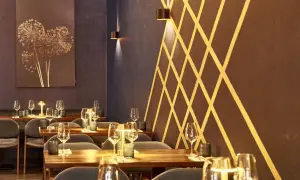 Stilvolles Ambiente im Lovis Restaurant: gedeckte Tische mit Gläsern und Kerzen, dunkle Wände mit goldenem Muster und ein Kunstwerk mit getrockneten Blumen.
