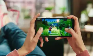 Dłonie trzymające smartfon z grą akcji w zielonym, bajkowym świecie.