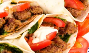 Kebab w tortilli z mięsem, pomidorami, zielonym sosem i majonezem.