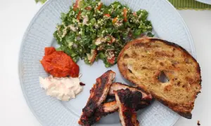En tallrik med grillade revbensspjäll, rostat bröd, en krämig sallad och en fräsch tabbouleh. Perfekt för ett somrigt tabbouleh recept.