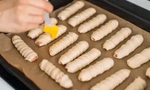 Parówki zawinięte w ciasto francuskie na blasze, przygotowywane do pieczenia.