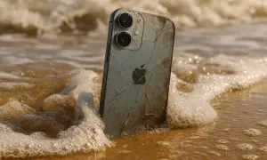 Un iPhone 12, malgré sa résistance à l'eau, est échoué sur une plage, les vagues léchant son dos fissuré.