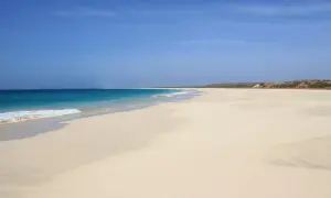 Pusta, piaszczysta plaża z turkusową wodą i błękitnym niebem.