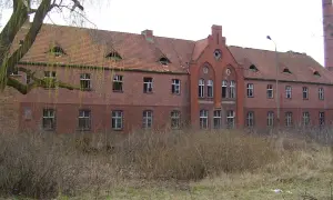 Opuszczony ceglany budynek z charakterystycznymi lukarnami i kominem. Wygląda jak jedno z tych strasznych miejsc, które kryją mroczne historie.