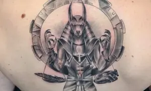 Tatuaje de Anubis con balanza, pluma y corazón, rodeado por un círculo mecánico.