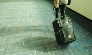 Osoba ciągnie czarną walizkę Smartwings po wzorzystej, niebiesko-szarej wykładzinie.