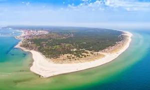 Malownicze wybrzeże pomorza gdańskiego z piaszczystą plażą, lasem sosnowym i miasteczkiem nad zatoką.