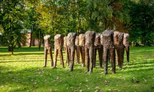 Rzeźby Magdaleny Abakanowicz, grupa bezgłowych postaci, stoi na trawiastym, jesiennym dziedzińcu.