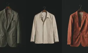 Drei Sakkos in Olivgrün, Beige und Rostrot hängen an Kleiderbügeln. Sie repräsentieren die **slow fashion definition**: zeitlose Designs, hochwertige Materialien und Langlebigkeit.