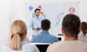 Nauczyciel prowadzi kurs reedukacyjny, tłumacząc zasady ruchu drogowego na tablicy. Uczestnicy słuchają uważnie.