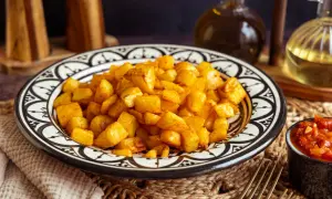Goldbraune Kartoffelwürfel, perfekt für ein Patatas Bravas Rezept, serviert auf einem marokkanisch inspirierten Teller. Daneben eine Schale mit würziger Tomatensauce.