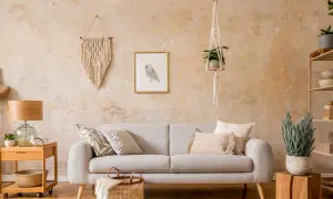 Gemütliches Wohnzimmer mit beiger Couch, Makramee-Wandbehang und einer Wand in Wischtechnik.