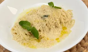 Spaghetti al limone, conditi con parmigiano grattugiato, olio d'oliva e guarniti con foglie di menta fresca.