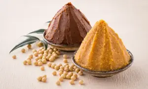 Dwa stożki pasty miso, jasnej i ciemnej, w miseczkach, obok ziaren soi i liści. Co to miso?