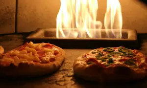 Deux pizzas maison, une à l'ananas et jambon, l'autre aux poivrons verts, cuisent dans un four avec des flammes vives. Une recette pizza maison avec pâte toute prête facile et rapide.