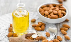 Aceite de almendras en botella, almendras en cuenco y esparcidas. El aceite de almendras mancha la piel con el sol, ¡pero nutre!