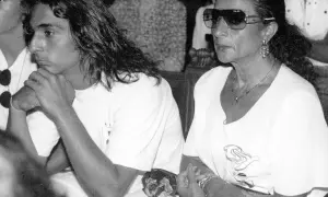 Un joven con pelo largo y una mujer con gafas de sol y joyas, sentados juntos. La imagen evoca la tristeza y el misterio en torno a como murio Lola Flores.