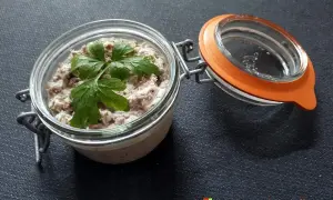 Un bocal ouvert révèle de délicieuses rillettes de sardines, garnies d'une feuille de persil frais.