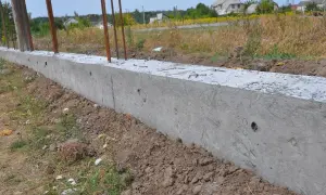 Betonowy fundament z prętami zbrojeniowymi. Czy można postawić płot przy płocie? Tu powstaje podstawa pod nowy.