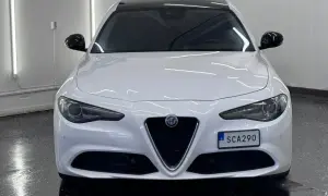 Vit Alfa Romeo Giulia, en elegant begagnad bil med mörk tak och svarta backspeglar. Perfekt för dig som söker stil och prestanda.