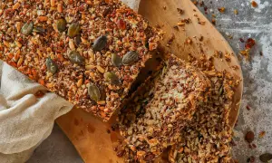 Brot ohne Mehl, reich an Saaten wie Kürbis- und Leinsamen, liegt auf einem Holzbrett.