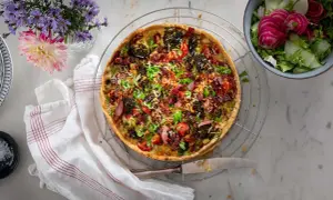 En gyllene quiche lorraine med broccoli, bacon och tomater, serverad med en fräsch sallad.