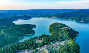 Widok z lotu ptaka na jezioro otoczone lasami, z widocznymi zabudowaniami i zaporą.
