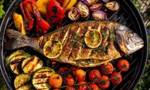 Une parillada de poisson grillé avec des légumes colorés : poivrons, courgettes, tomates cerises et oignons. Des rondelles de citron et des herbes aromatiques complètent ce plat savoureux.