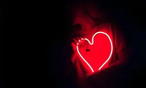 Een persoon houdt een gloeiend rood neonhart vast. Dit is wat ontgroend liefde kan voelen: warm, helder en vol passie.