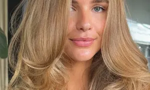 Piękna kobieta z falowanymi włosami w odcieniu maślany blond. Jej oczy są zielone, a usta delikatnie umalowane.