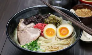 Parujący makaron do ramen z plastrami wieprzowiny, jajkiem na pół, szczypiorkiem i marynowanymi dodatkami.