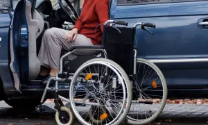 Osoba w wózku inwalidzkim obok otwartych drzwi samochodu. Ułatwia to wsiadanie i wysiadanie, zapewniając ulgę na samochód.