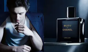 Młody mężczyzna w garniturze i podkoszulku, obok flakonik perfum BLEU DE CHANEL L'EXCLUSIF.