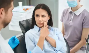 Pacjentka z bólem zęba, wskazująca na policzek, martwiąca się powikłaniami po szlifowaniu zębów. Obok dentysta i asystentka.