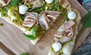 En läcker pinsa pesto med mortadella, mozzarella, pistagenötter och färsk basilika på en träskärbräda.