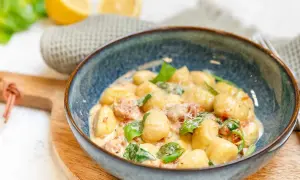 En skål med krämig gnocchi salsiccia, toppad med färsk basilika och parmesan. Citroner och en grå handduk i bakgrunden.
